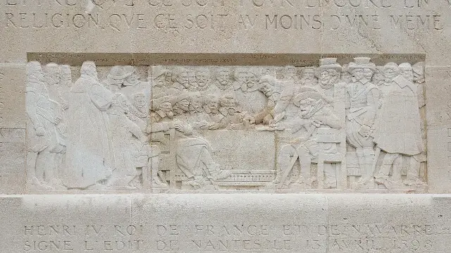 Stone bas-relief on Geneva's Reformation Wall showing Henri IV of France signing the Edict of Nantes in 1598, with a carved inscription below noting the edict was signed on April 13, 1598
