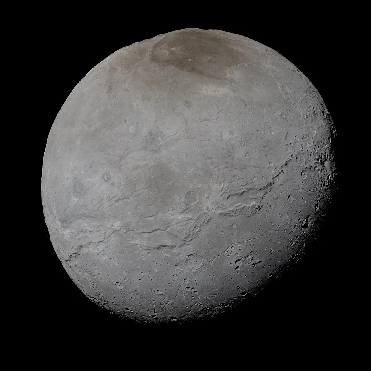 Pluto's moon Charon in enhanced true color, a gray cratered sphere with a dark reddish region across its north pole.