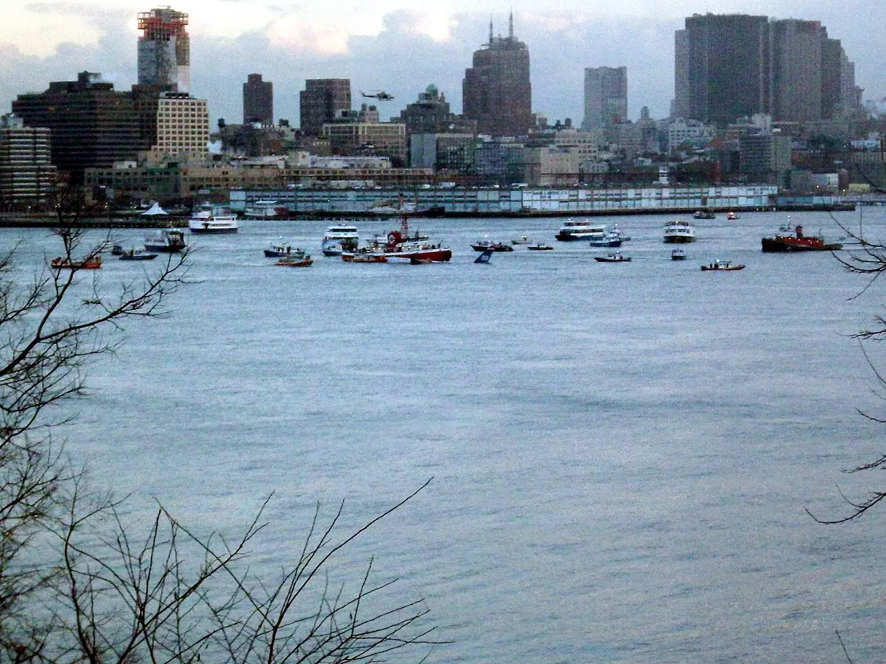 Rescue boats surrounding the tail of US Airways Flight 1549 floating in the Hudson River with the Manhattan skyline behind