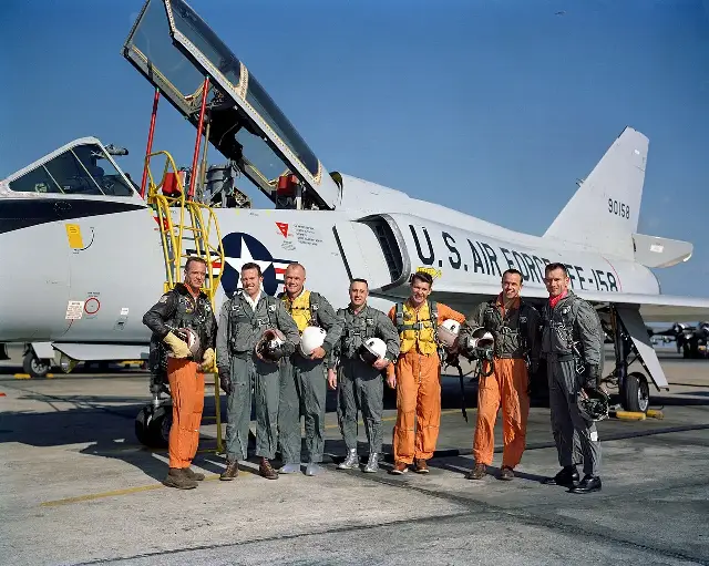The seven Mercury astronauts in flight suits posing beside a U.S. Air Force jet.