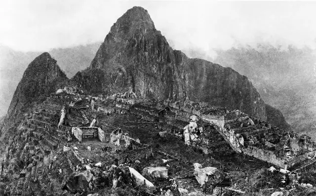 An early black-and-white photograph of Machu Picchu taken by Hiram Bingham III, showing the stone ruins with Huayna Picchu peak behind