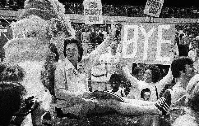 Billie Jean King, smiling and waving, being carried into the Houston Astrodome on a gold litter before the 1973 Battle of the Sexes, as fans hold up signs