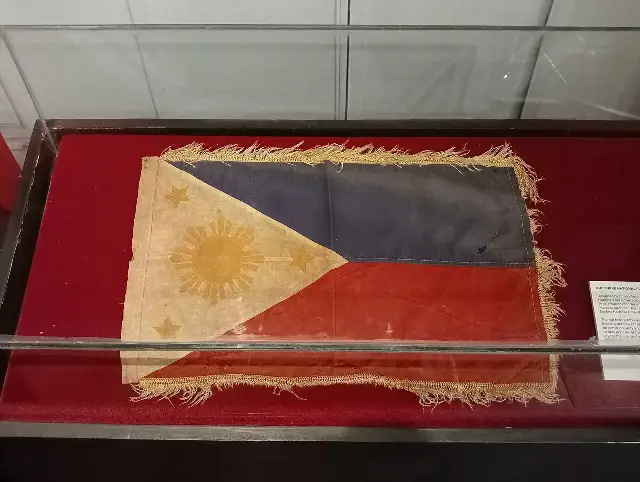The original Philippine national flag, unfurled during the June 12, 1898 independence proclamation, preserved in a display case at the Aguinaldo Shrine in Kawit, Cavite.