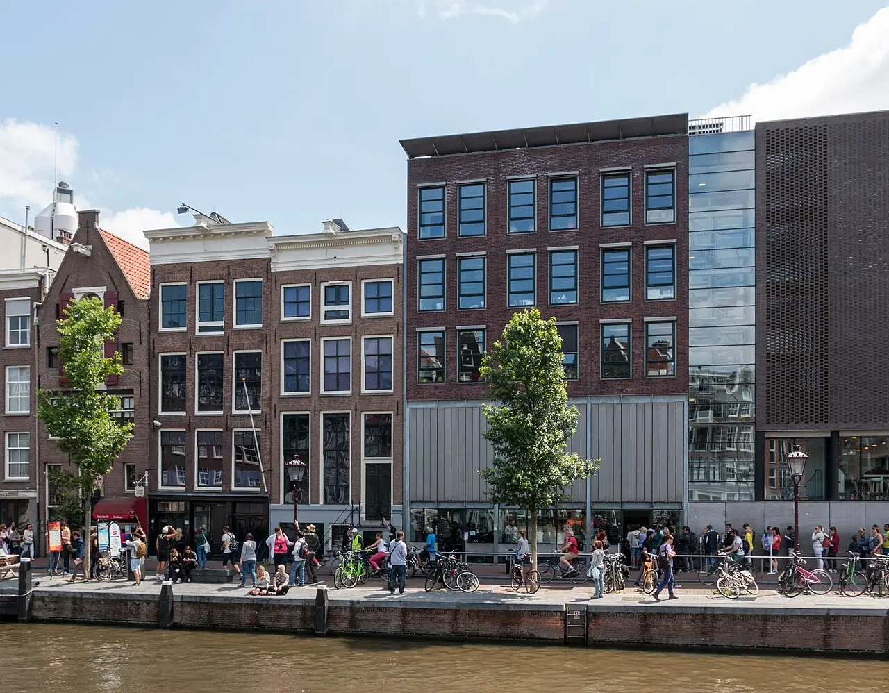 The Anne Frank House on the Prinsengracht canal in Amsterdam, with visitors and bicycles along the waterfront in front.