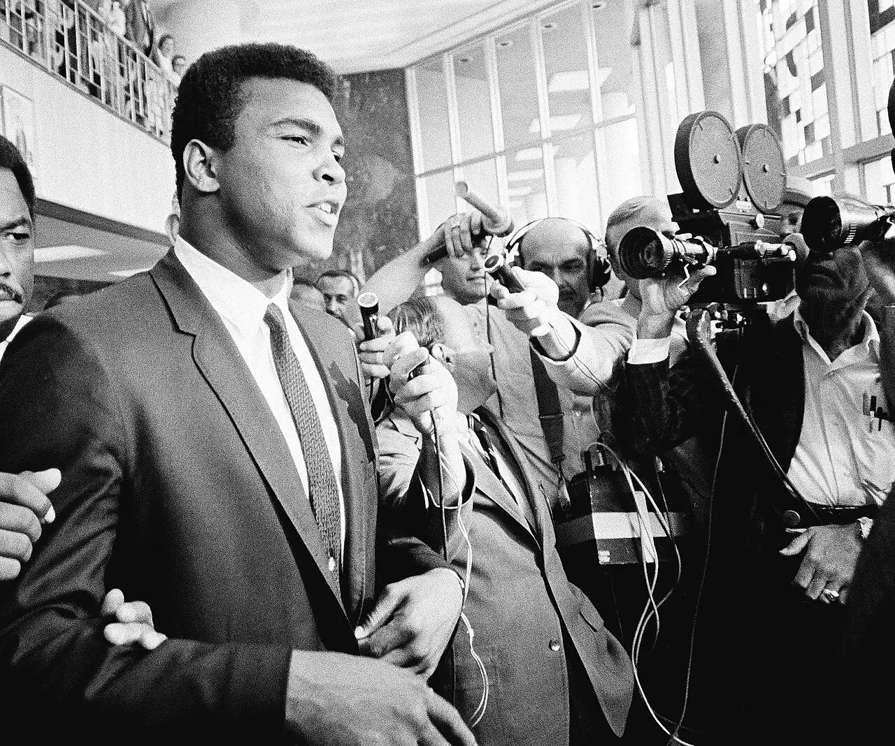 Muhammad Ali leaving a Houston courthouse during his 1967 draft-evasion trial, surrounded by reporters and cameras — an illustrative photo from the months after his refusal of induction, not the induction itself.