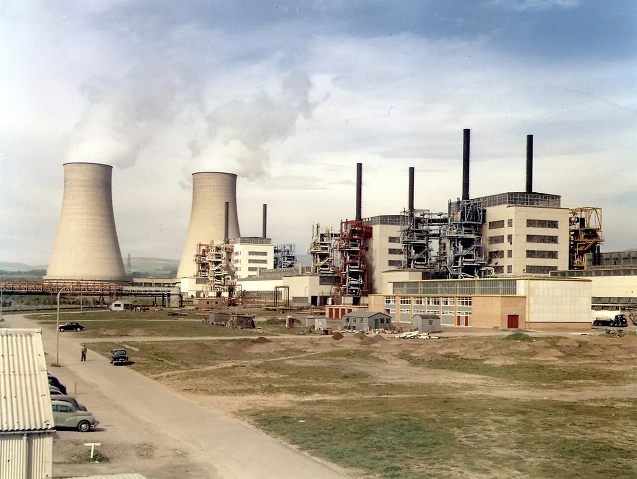 A color photograph of Calder Hall nuclear power station in Cumbria shortly after opening, showing reactor buildings and tall cooling towers under a cloudy sky.