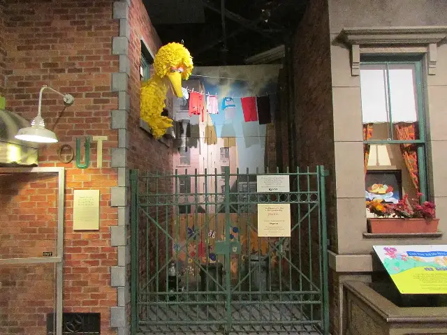 Illustrative: the Sesame Street set exhibit at the National Museum of Play in Rochester, New York, with Big Bird leaning from a window above the show's iconic green fence.