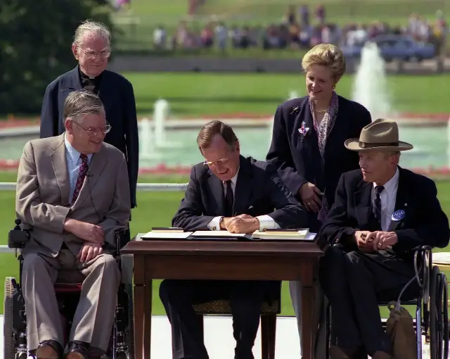 President George H. W. Bush signs the Americans with Disabilities Act on the White House South Lawn, July 26, 1990, flanked by disability advocates.
