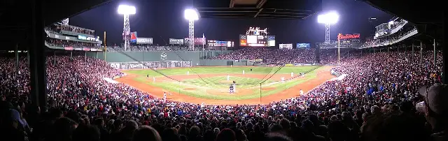 A panoramic view of Fenway Park at night during a game, with a packed crowd under the stadium lights.