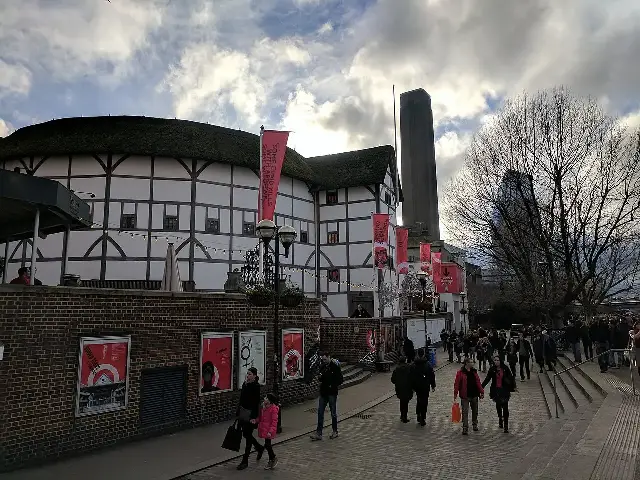 The reconstructed Shakespeare's Globe Theatre in London, a white timber-framed playhouse with a thatched roof, seen from the riverside walkway.