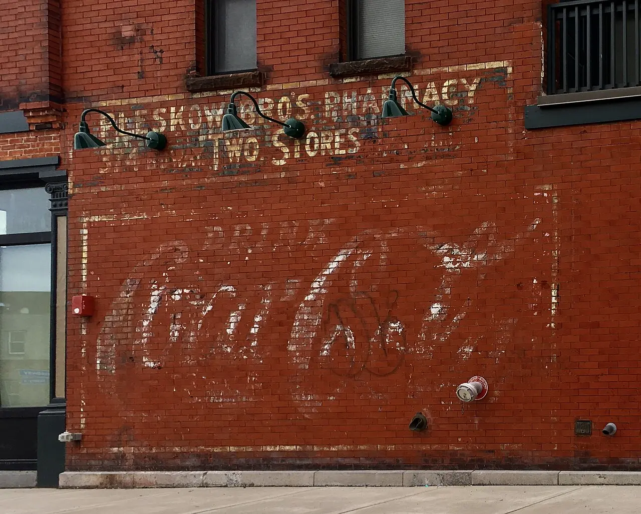A faded vintage Coca-Cola advertisement painted on the brick wall of a former pharmacy — an echo of the drink's soda-fountain origins.