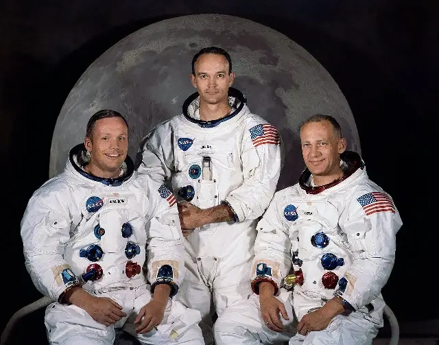 The Apollo 11 crew — Neil Armstrong, Michael Collins, and Buzz Aldrin — in their spacesuits against a backdrop of the Moon.