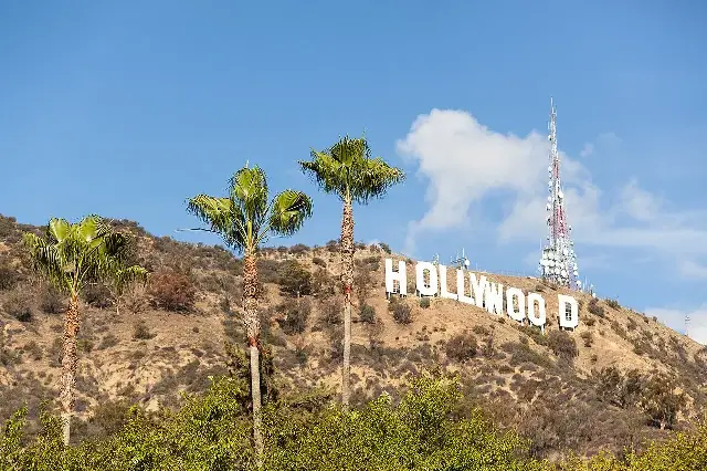 The Hollywood sign on Mount Lee above Los Angeles, with palm trees in the foreground.
