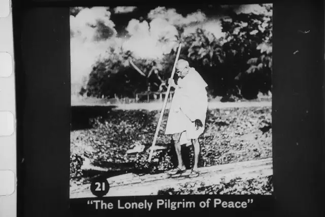 A 1946 newsreel still captioned 'The Lonely Pilgrim of Peace,' showing Gandhi walking barefoot with a long staff through fields in Noakhali.