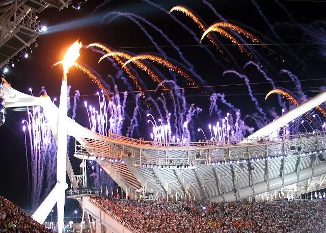 The Olympic flame burns above the stadium during the Athens 2004 opening ceremony, with fireworks overhead.