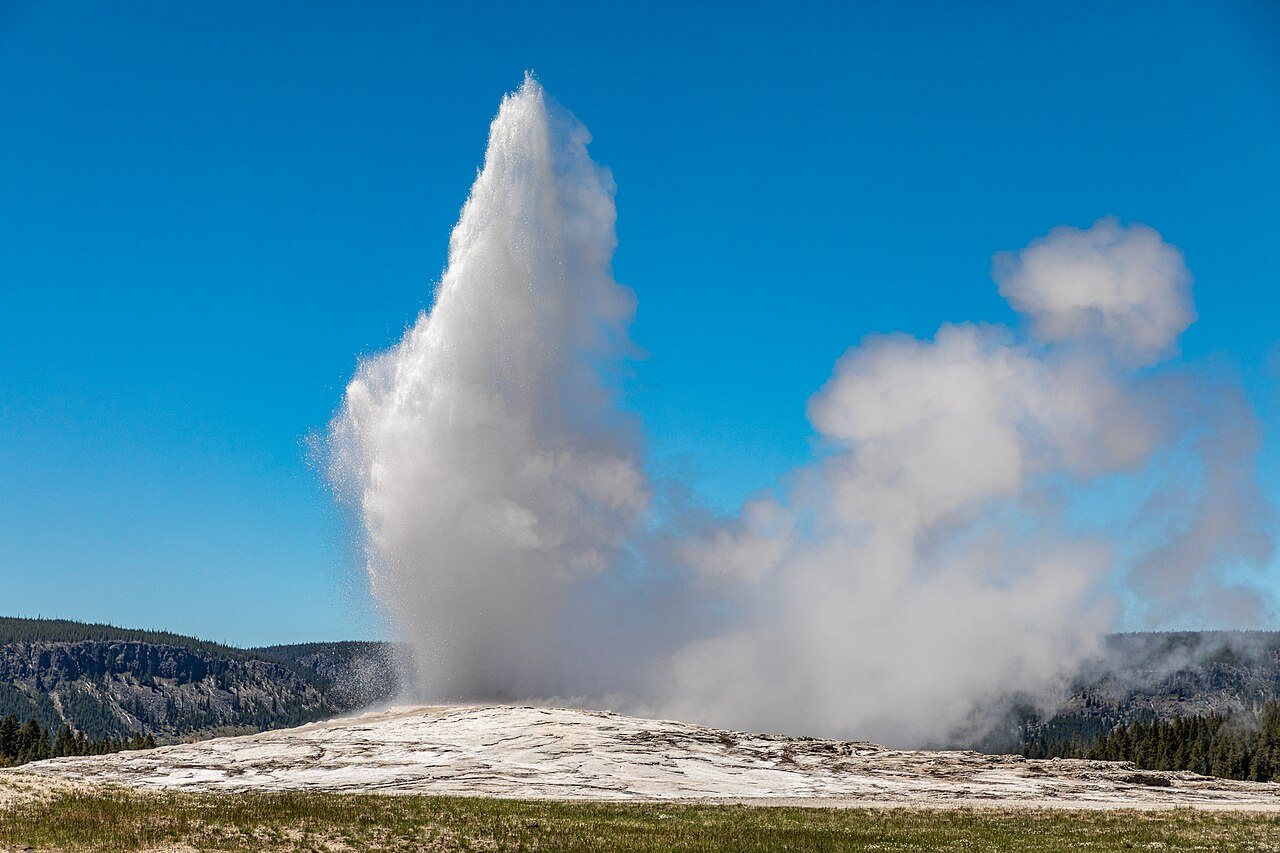 Old Faithful geyser erupting under a clear blue sky in Yellowstone National Park.