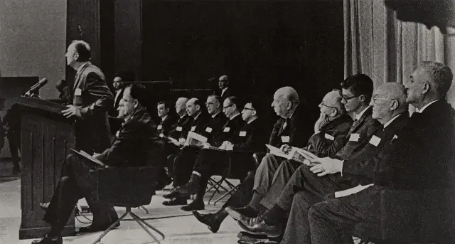 Surgeon General Luther Terry speaking at a podium during the January 11, 1964 press conference releasing the report on smoking and health, with committee members seated behind him.