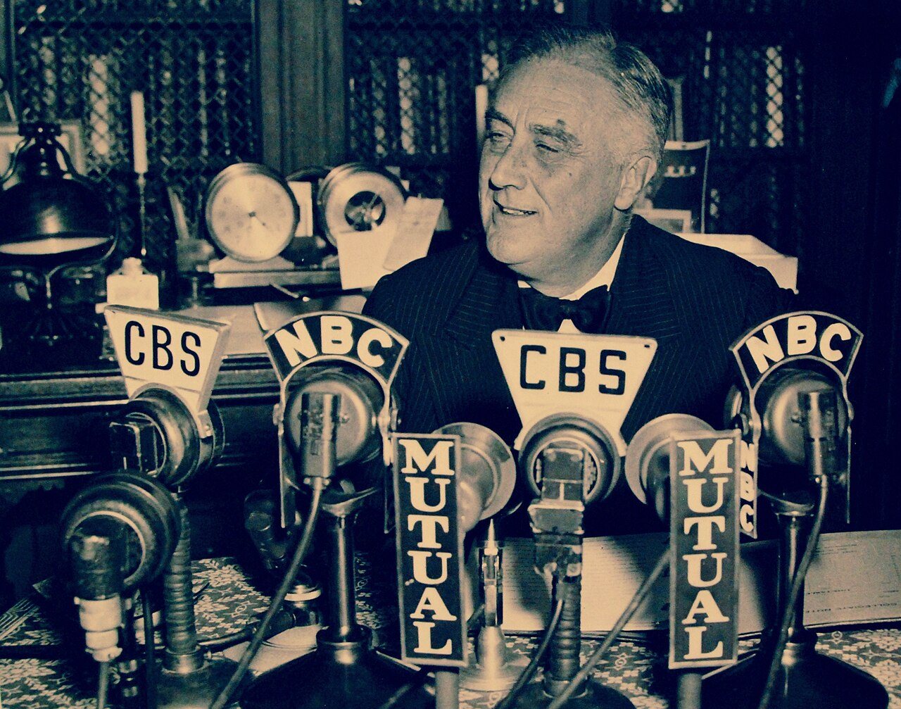 President Franklin D. Roosevelt broadcasting a radio address from his home in Hyde Park, New York, on November 4, 1938, surrounded by CBS, NBC, and Mutual network microphones.