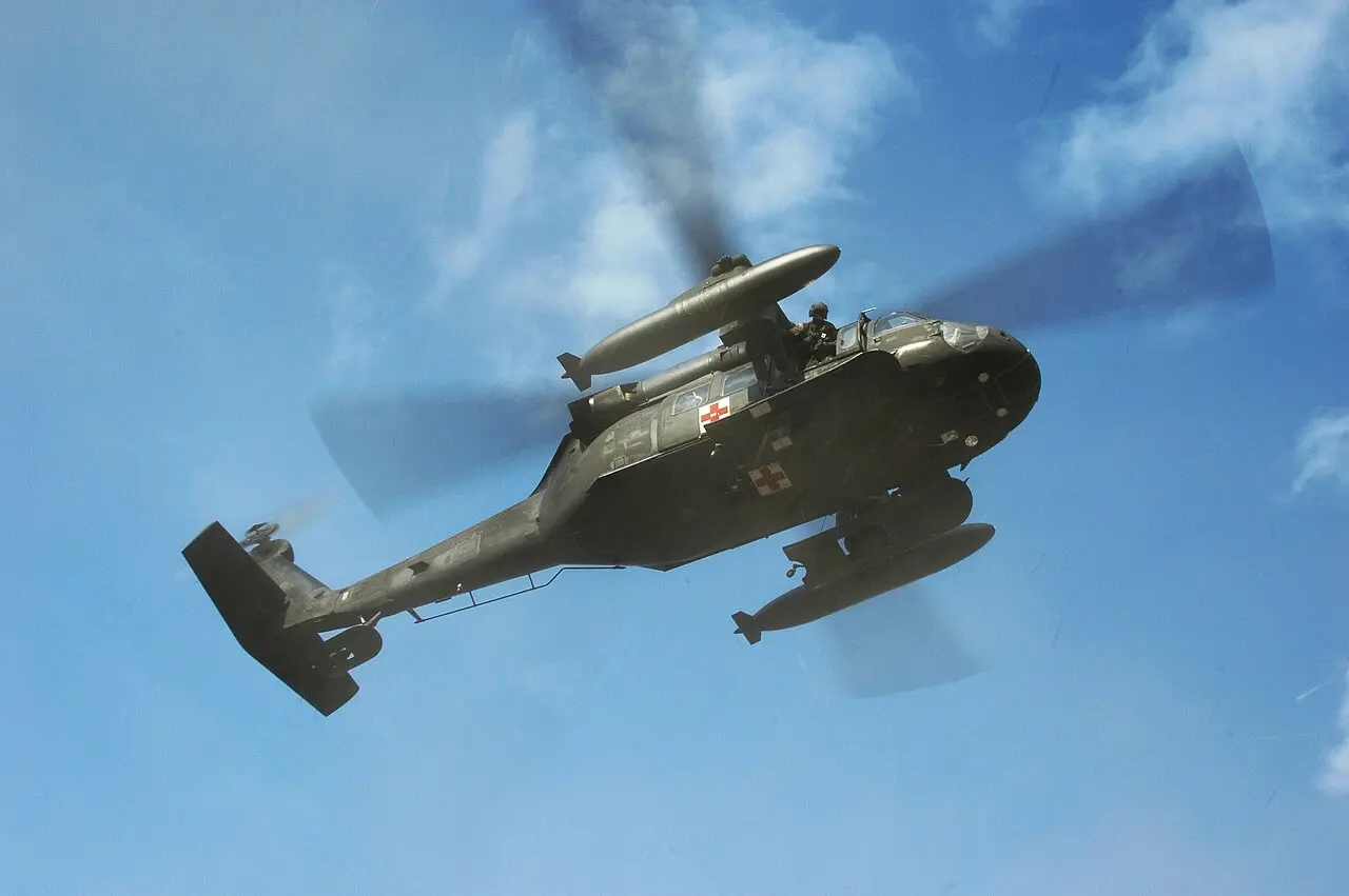 A U.S. Army UH-60 Black Hawk helicopter in flight against a blue sky, bearing red-cross medical markings