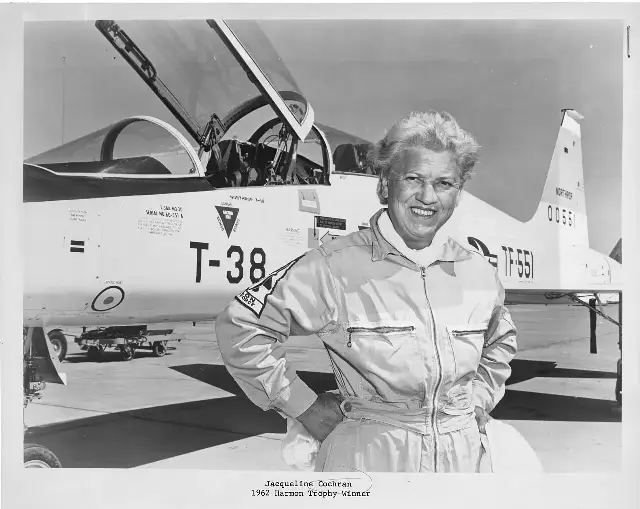 Jacqueline Cochran, 1962 Harmon Trophy winner, standing beside a jet in her flight suit.
