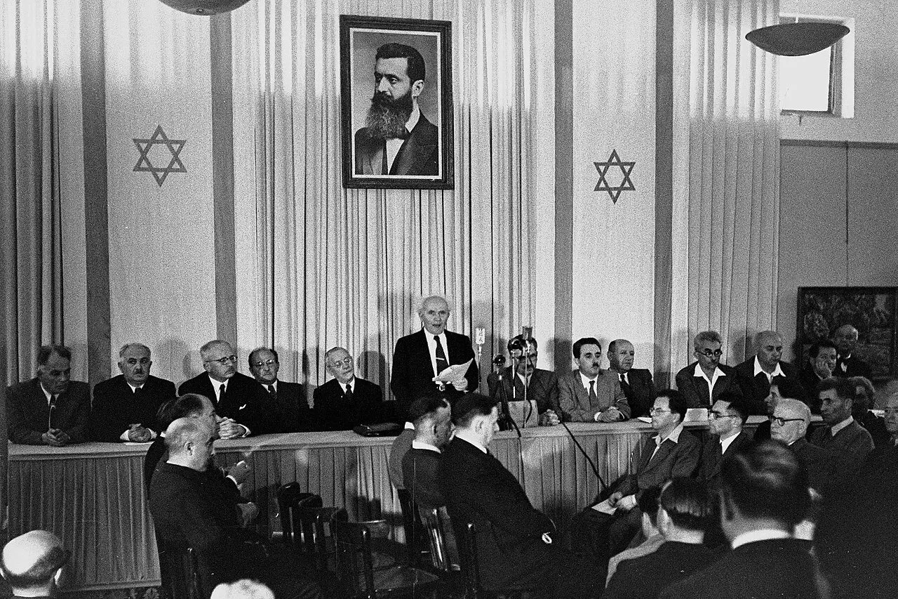 David Ben-Gurion reading the Declaration of Independence at the Tel Aviv Museum on May 14, 1948, under a portrait of Theodor Herzl.