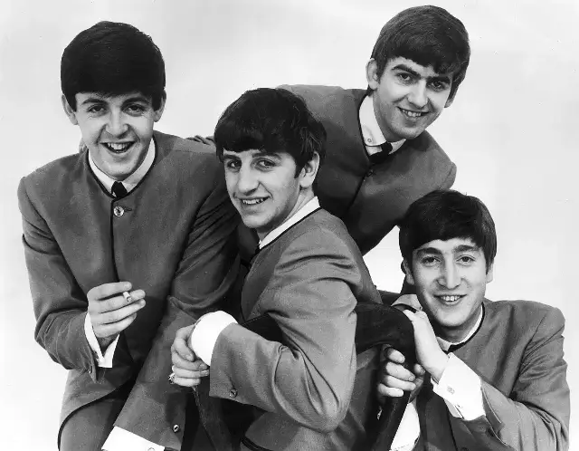Black-and-white 1963 publicity photo of the four Beatles smiling in collarless suits.