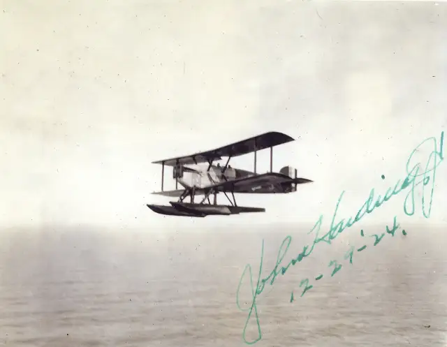 A 1924 photograph of a Douglas World Cruiser biplane on floats in flight over the ocean, signed by crew member John Harding Jr.