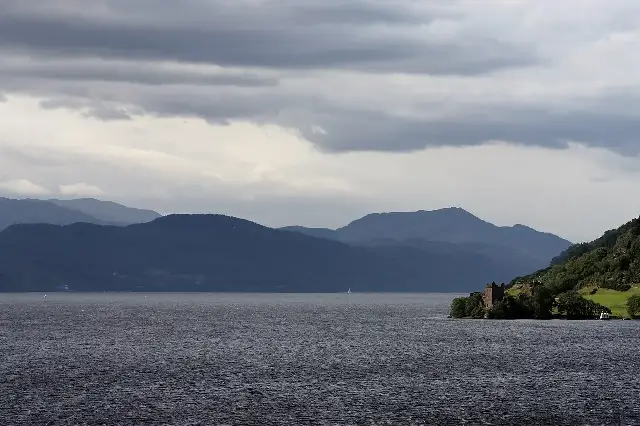 Loch Ness with the ruins of Urquhart Castle on its shore under a moody sky