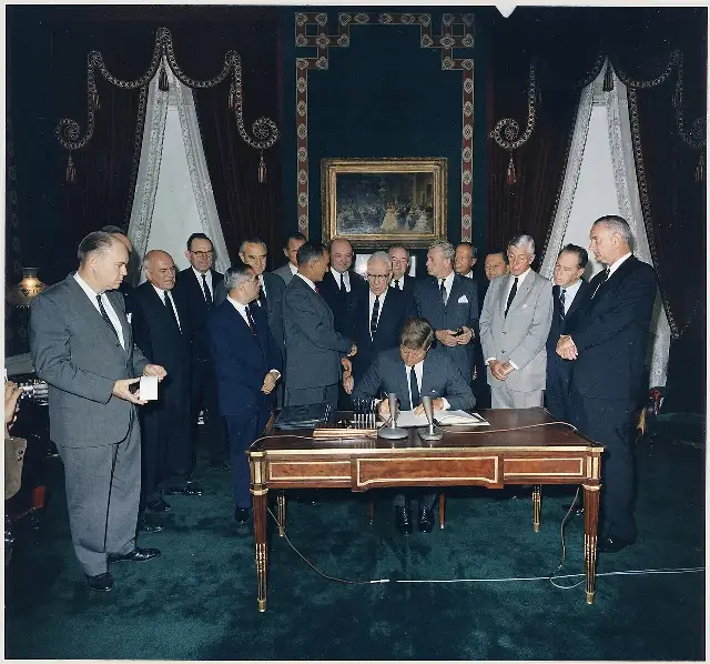 President John F. Kennedy signing the instruments of ratification of the Limited Nuclear Test Ban Treaty in the White House Treaty Room on October 7, 1963, flanked by Vice President Lyndon Johnson, Secretary of State Dean Rusk, and senators.