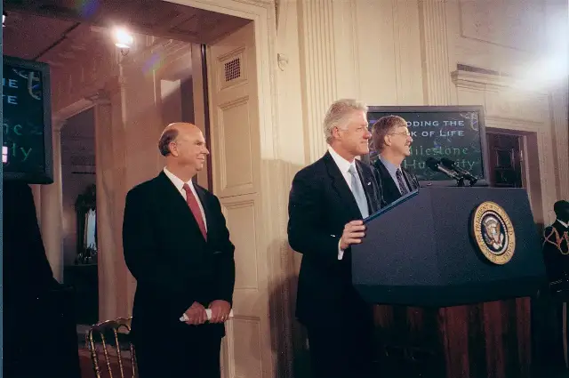 President Bill Clinton speaking at a White House podium in June 2000 with Francis Collins of the National Human Genome Research Institute beside him, at the announcement of the working draft of the human genome