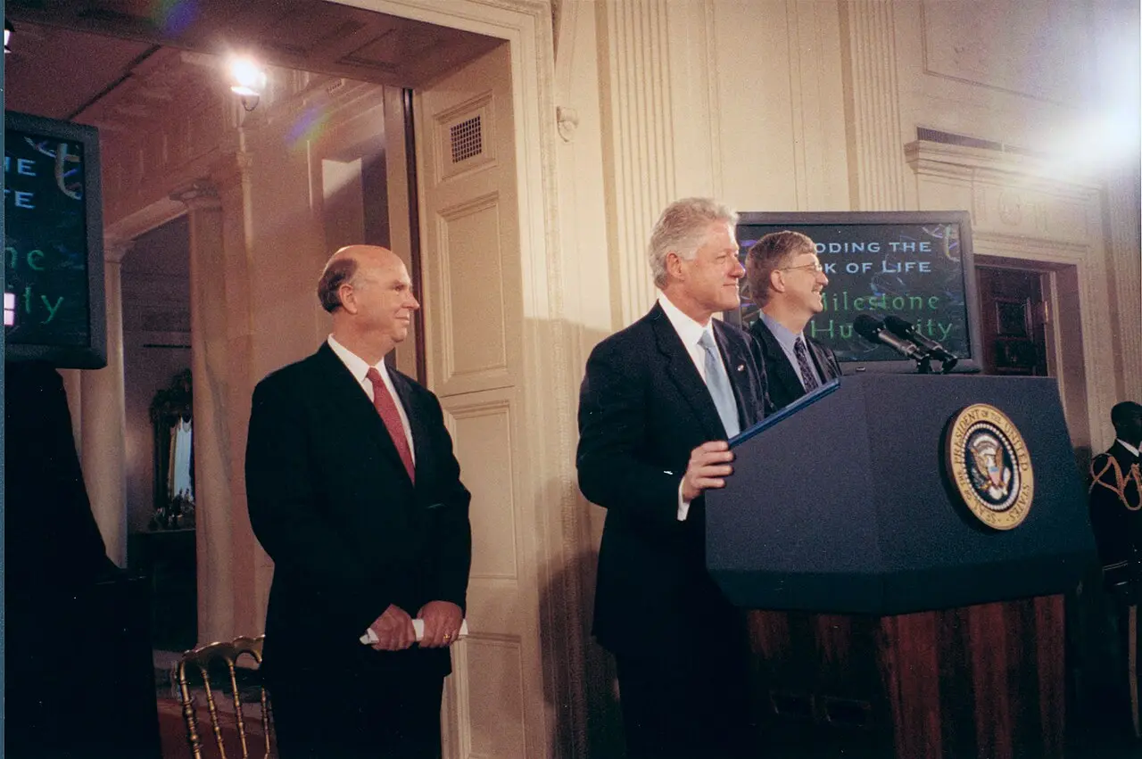 President Bill Clinton speaking at a White House podium in June 2000 with Francis Collins of the National Human Genome Research Institute beside him, at the announcement of the working draft of the human genome