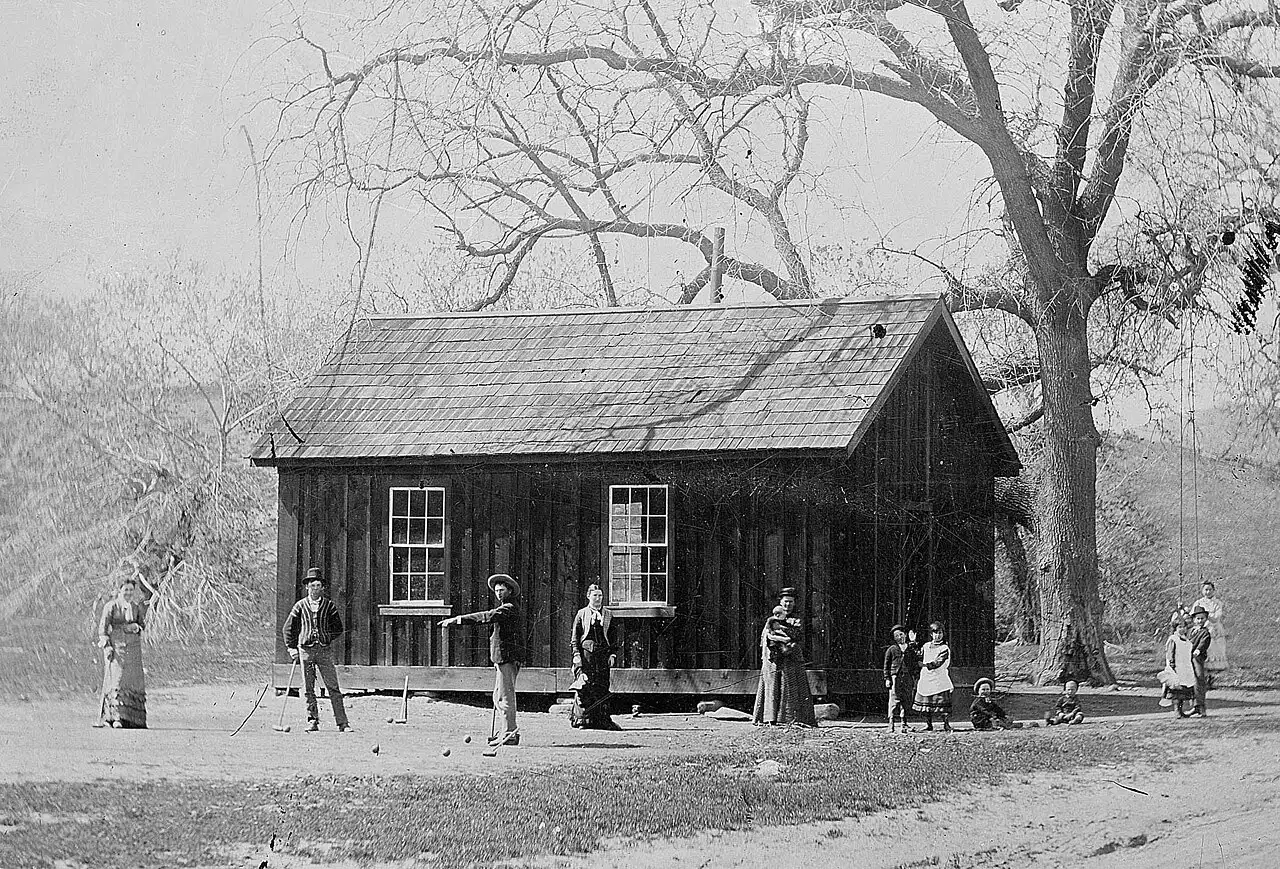 An 1881 tintype photograph showing Billy the Kid playing croquet with others outside a wooden building in New Mexico.