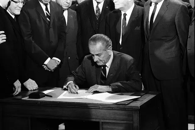 President Lyndon B. Johnson signing the Civil Rights Act of 1968 at a desk, surrounded by members of Congress, on April 11, 1968
