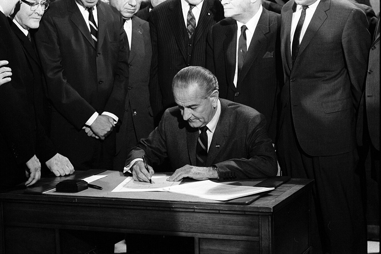 President Lyndon B. Johnson signing the Civil Rights Act of 1968 at a desk, surrounded by members of Congress, on April 11, 1968