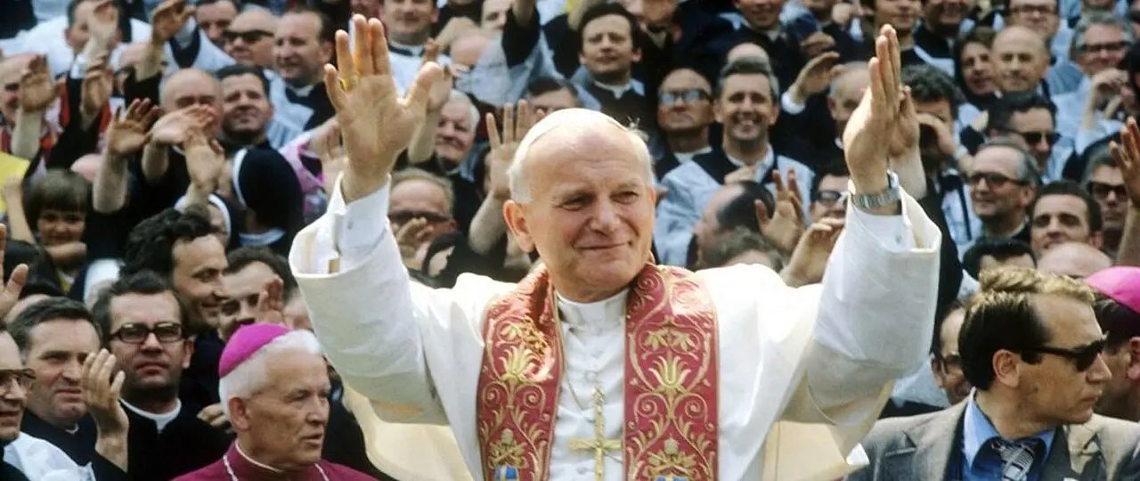 Pope John Paul II, smiling and raising both hands in blessing, waves to a large cheering crowd during his 1979 visit to Poland.
