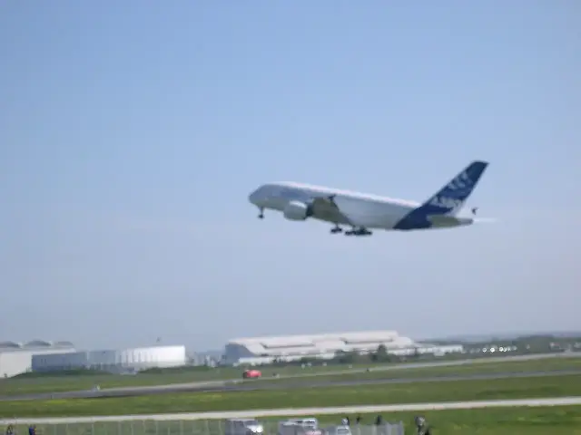 The Airbus A380 prototype climbing out of Toulouse-Blagnac airport on its maiden flight, April 27, 2005, landing gear still extended, its blue tail marked 'A380'.