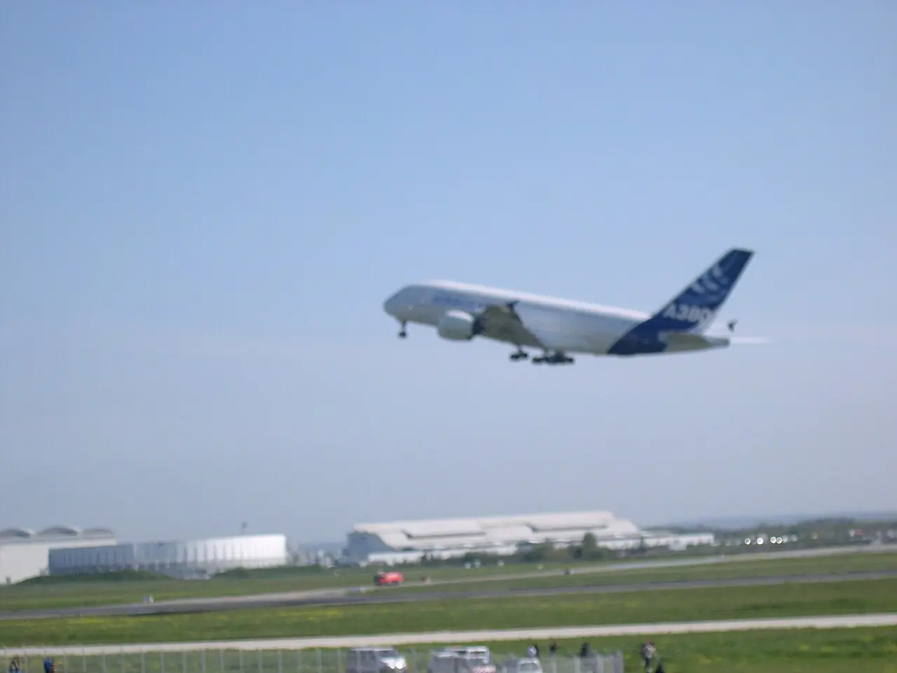 The Airbus A380 prototype climbing out of Toulouse-Blagnac airport on its maiden flight, April 27, 2005, landing gear still extended, its blue tail marked 'A380'.