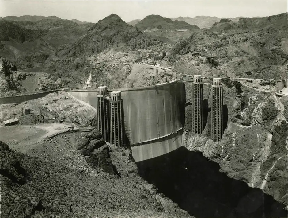 A 1935 black-and-white photograph of Hoover Dam's curved concrete face with its intake towers, set in the Black Canyon of the Colorado River