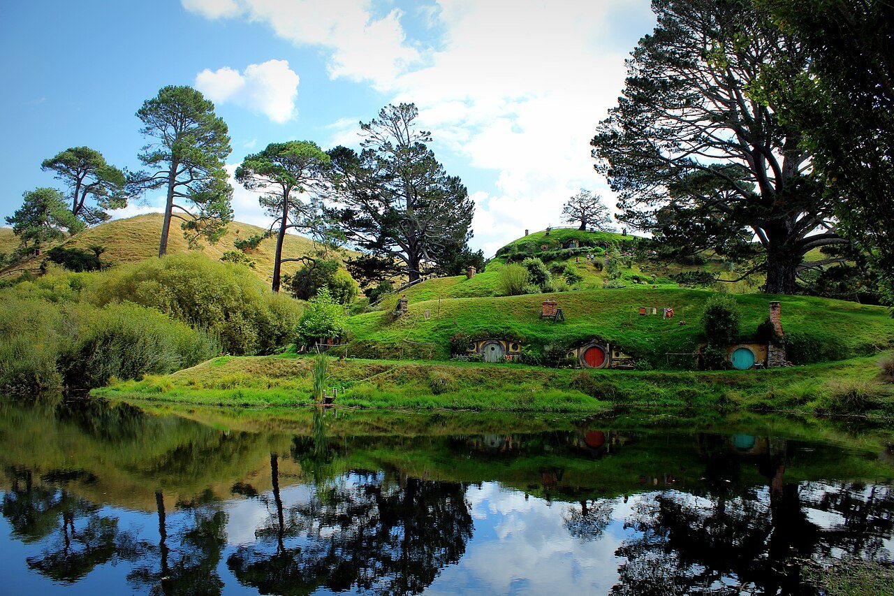 Round-doored hobbit holes at the Hobbiton movie set in New Zealand, reflected in still water