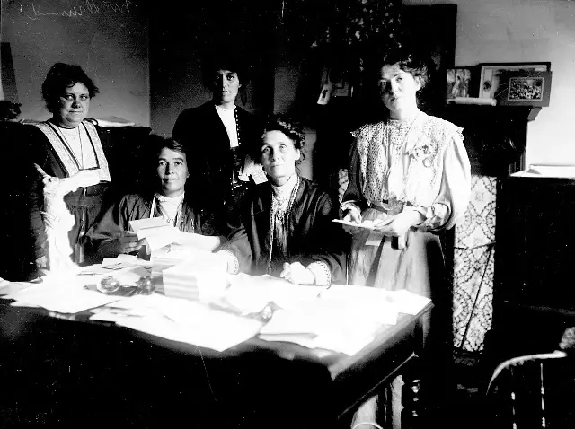 Emmeline Pankhurst and fellow suffragette leaders around a desk covered with papers in 1908
