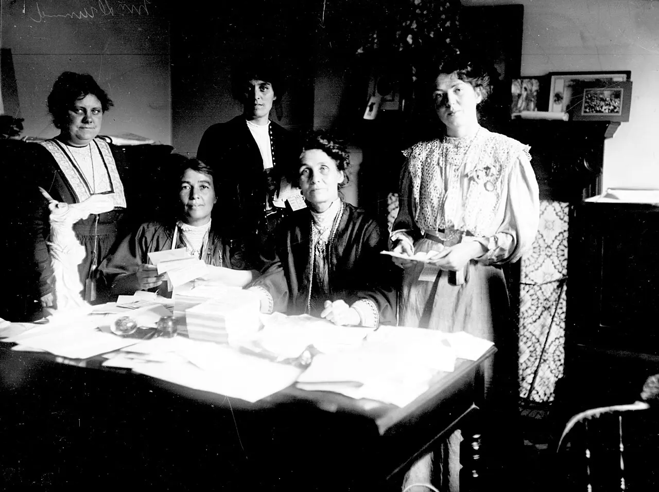 Emmeline Pankhurst and fellow suffragette leaders around a desk covered with papers in 1908