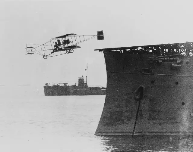 Eugene Ely's Curtiss Pusher biplane leaving the wooden platform on the bow of the USS Birmingham at the moment of the first shipboard takeoff, November 14, 1910.