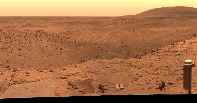Panoramic view of the Martian landscape at West Valley captured by NASA's Spirit rover, with the rover's solar-paneled deck visible at lower left and its camera mast at right.
