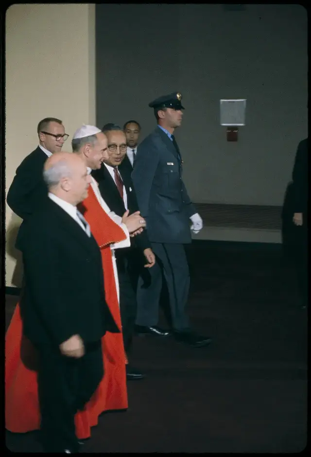 Color photograph of Pope Paul VI in white and red vestments walking with UN officials during his 1965 visit to the United Nations in New York