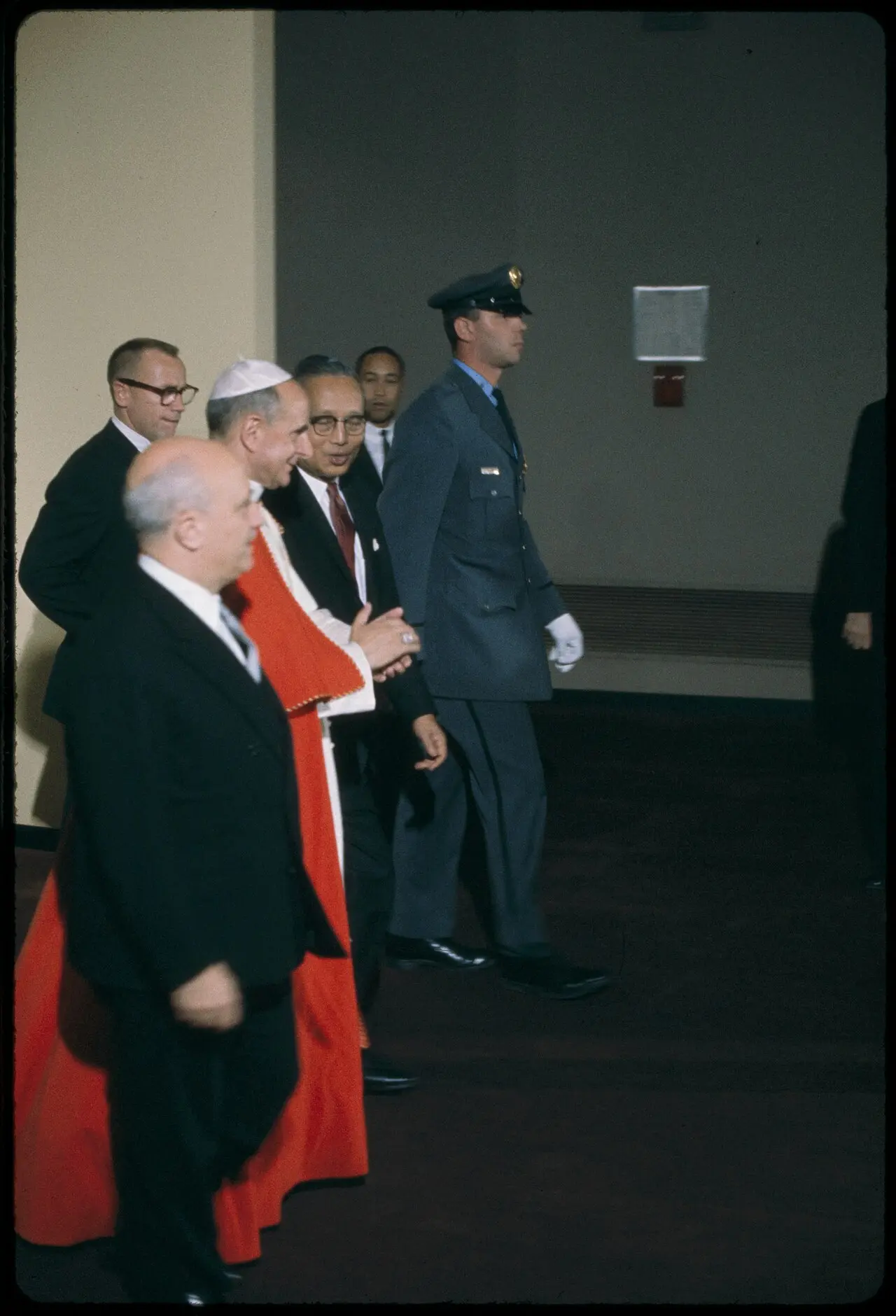Color photograph of Pope Paul VI in white and red vestments walking with UN officials during his 1965 visit to the United Nations in New York
