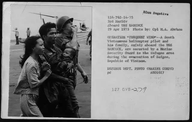 A U.S. Marine Corps photo dated April 29, 1975: a South Vietnamese helicopter pilot and his family, safely aboard the USS Hancock, escorted by a Marine security guard to the refugee area during the evacuation of Saigon.