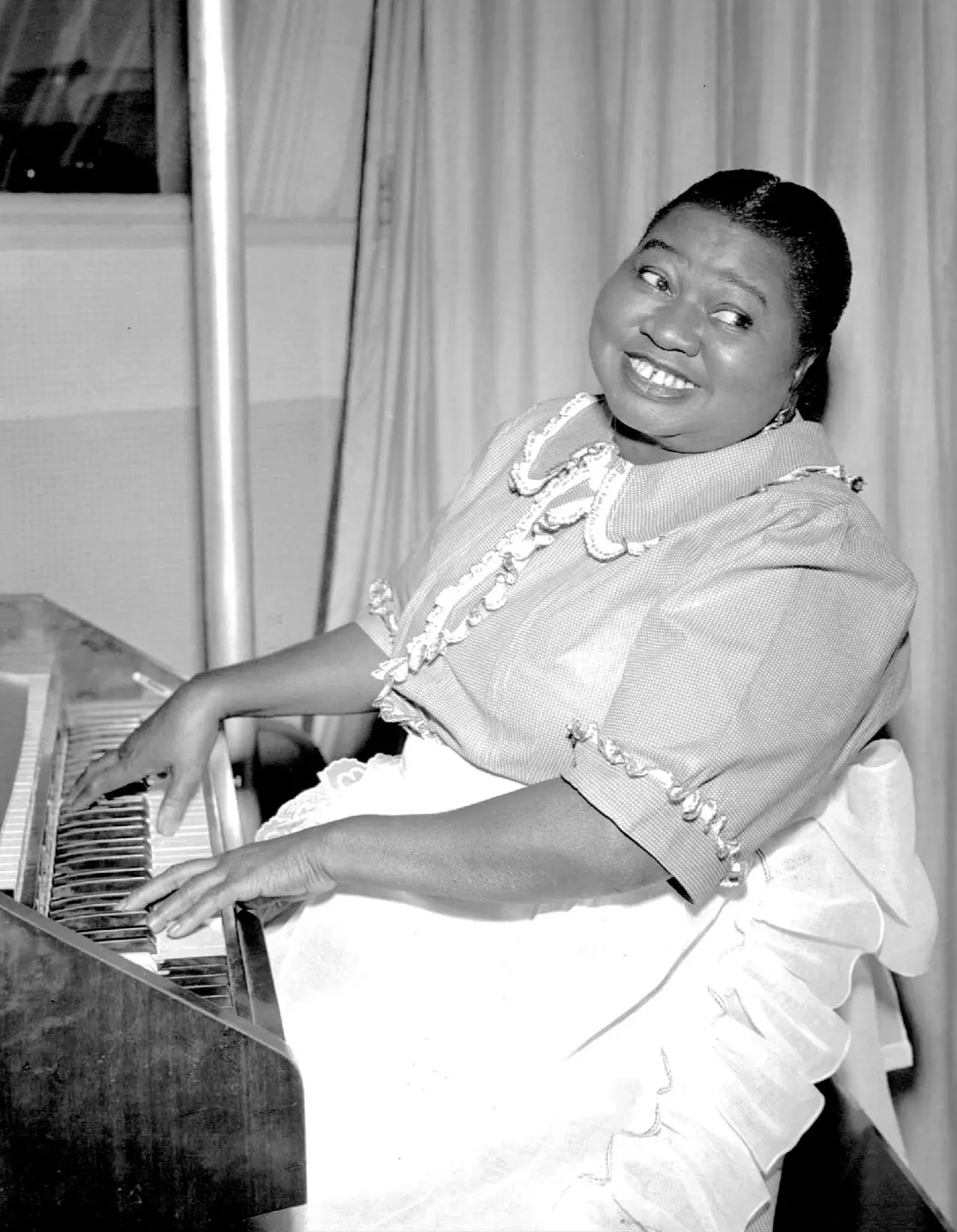 Hattie McDaniel smiling warmly while seated at a piano in a 1951 CBS Radio publicity photo