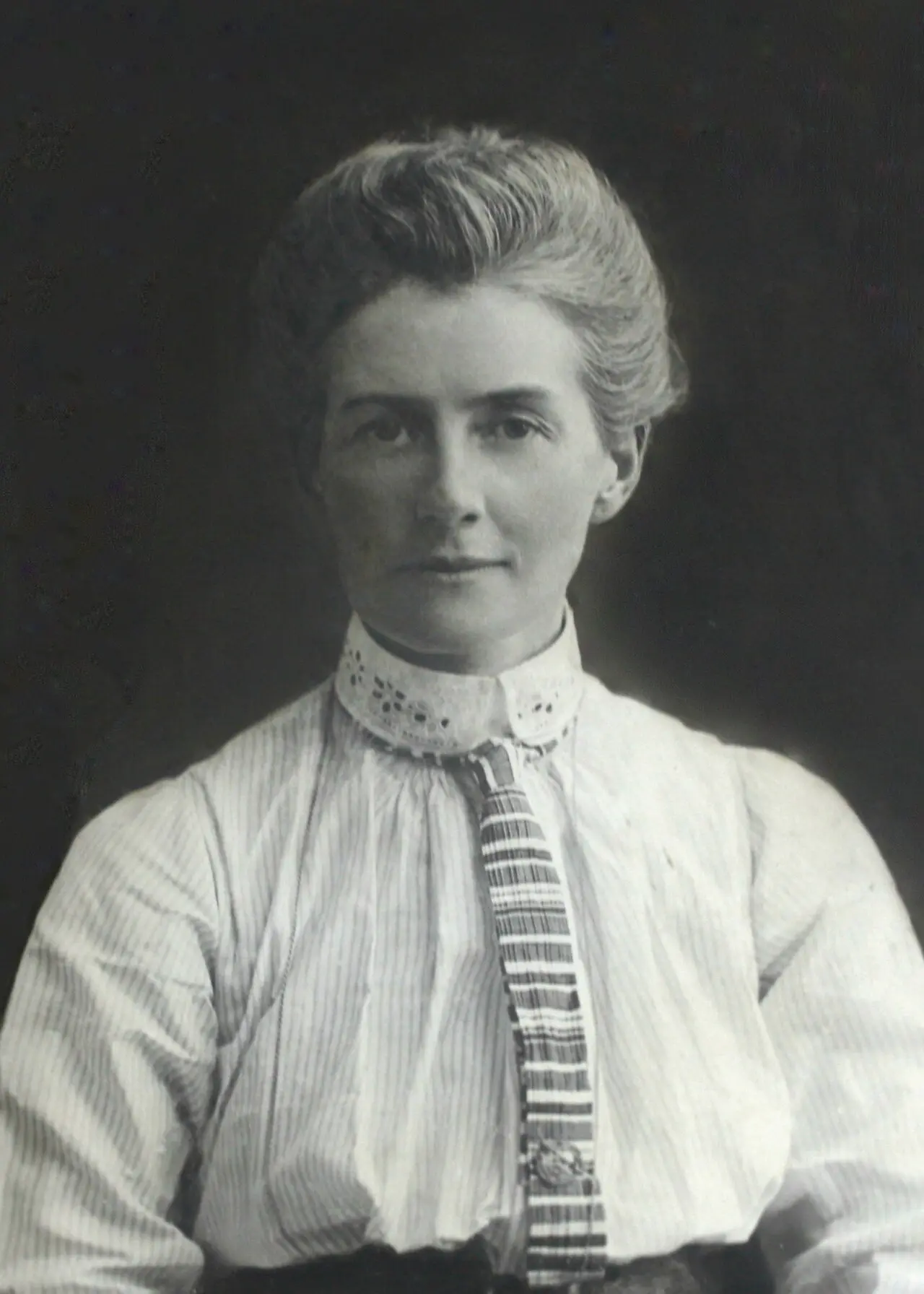A formal black-and-white studio portrait of nurse Edith Cavell, wearing a dark dress with a white collar and a Red Cross-style nurse's veil.