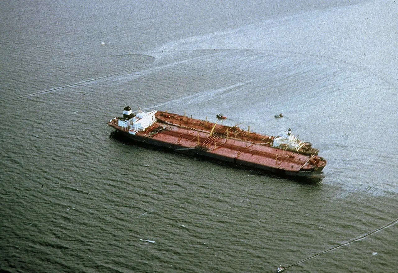 Aerial view of the grounded Exxon Valdez tanker with a visible slick of spilled oil spreading in the water around it.