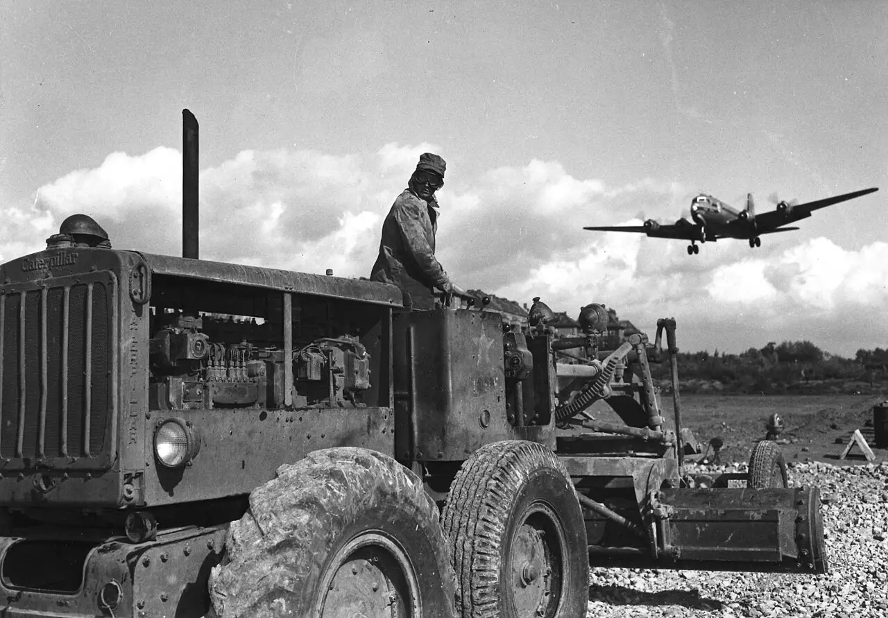 A C-54 Skymaster transport plane landing at Berlin's Tempelhof Airport during the 1948 Berlin Airlift, with a worker on a grader in the foreground.